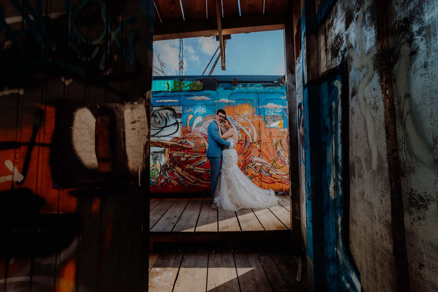 A couple in wedding clothes in front of a graffiti place in Munich hugging.