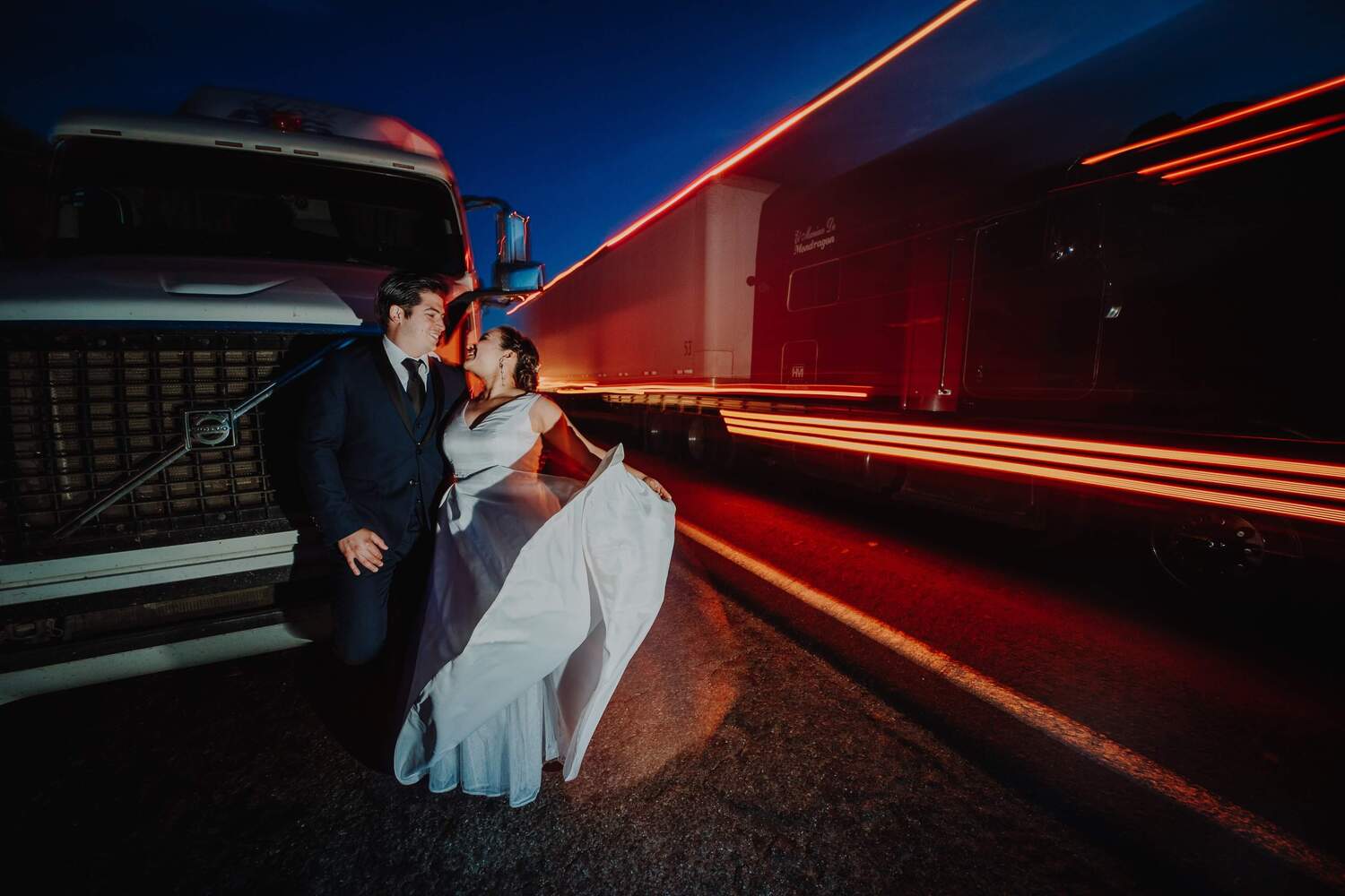 A couple standing in front of a truck while traffic is flowing behind them